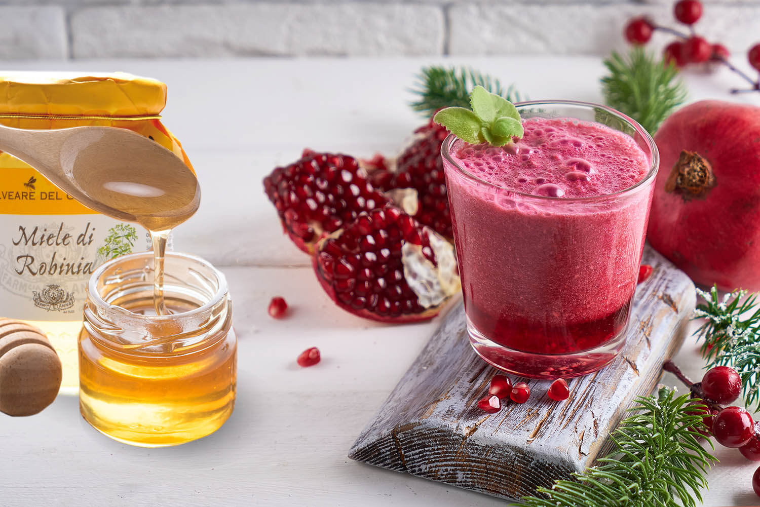 pomegranate smoothie in a glass on a white wooden table with fir branches and winter berries Copyspace
